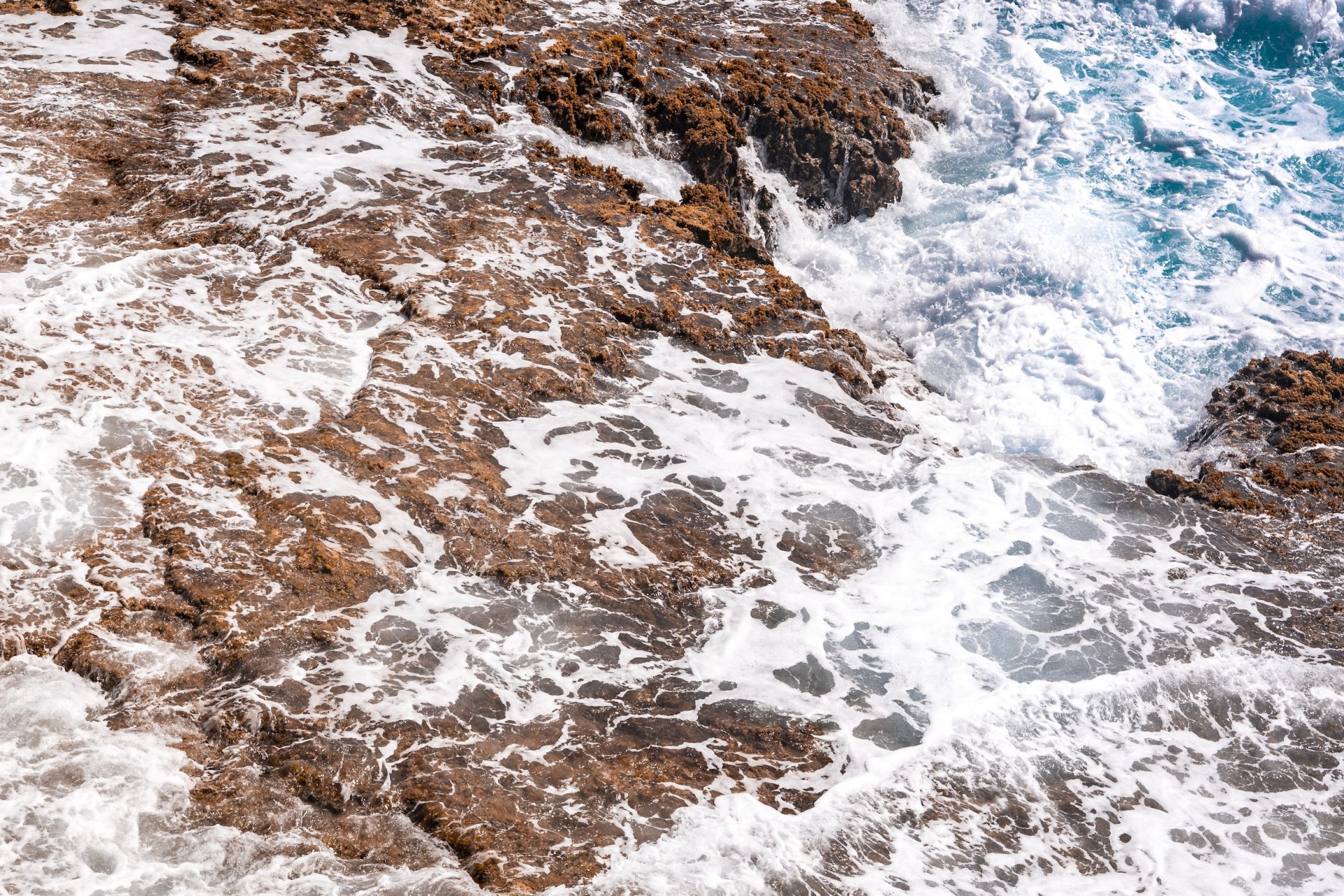 Waves washing white foam over rust-brown rocks at the shoreline, seen from above, Isla Mujeres, Mexico