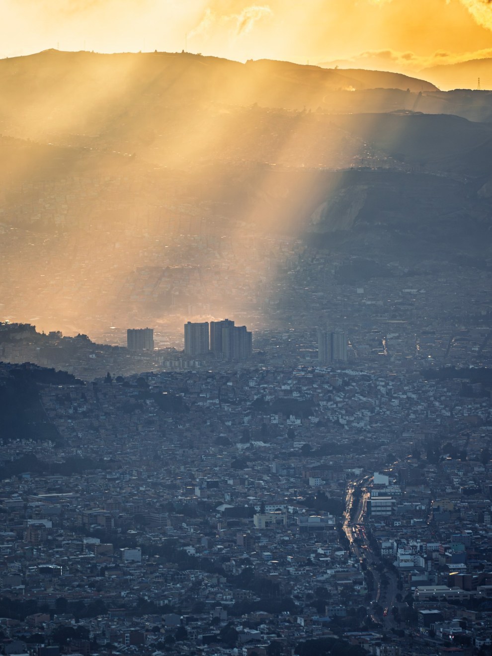 Sunbeams breaking through clouds over the mountains and the dense city of Bogotá, Colombia
