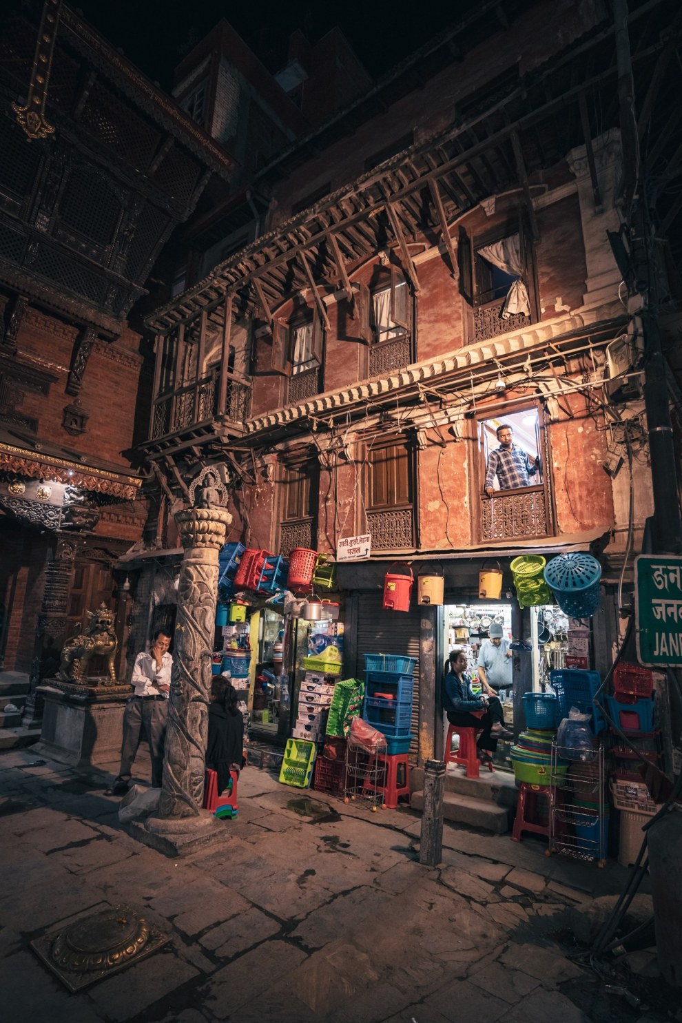 Small shop with colourful goods beneath an ornate carved wooden building at dusk, Kathmandu, Nepal