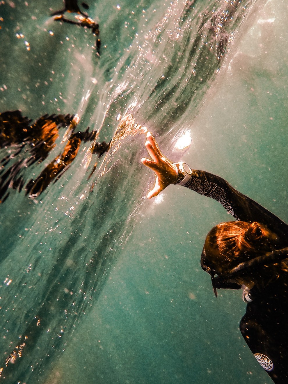 Swimmer reaching towards the sparkling water surface, seen from underwater in Moalboal, Philippines