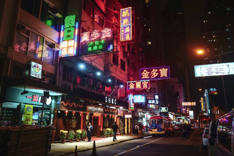 Street lined with red and green neon signs at night in Hong Kong