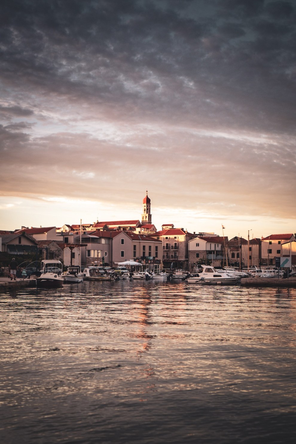 Harbour town of Betina on the island of Murter, Croatia, with a church tower reflected in calm water at sunset