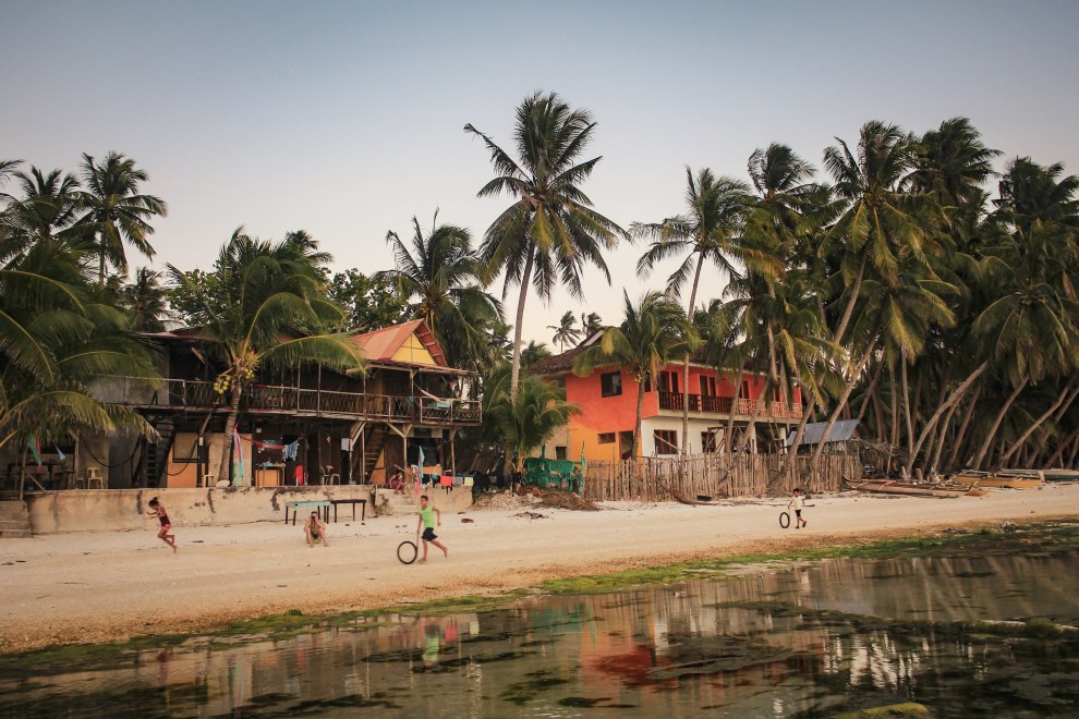 Palm-lined beach with wooden houses on Siquijor Island, Philippines, children playing with tyres on the sand at low tide