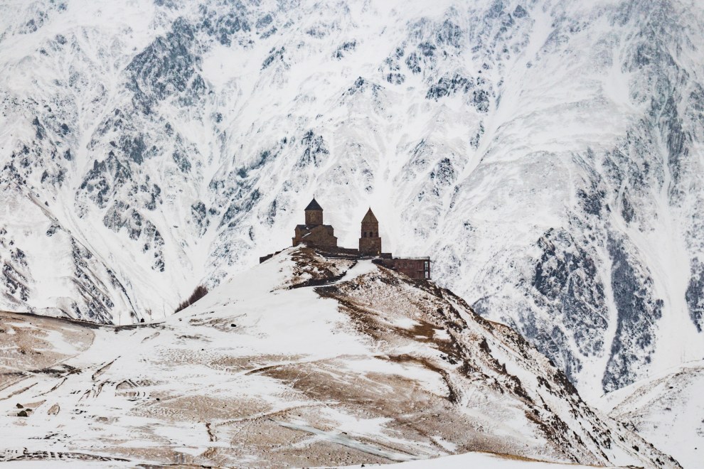Gergeti Trinity Church on a snowy hilltop in front of snow-covered mountains near Kazbegi, Georgia