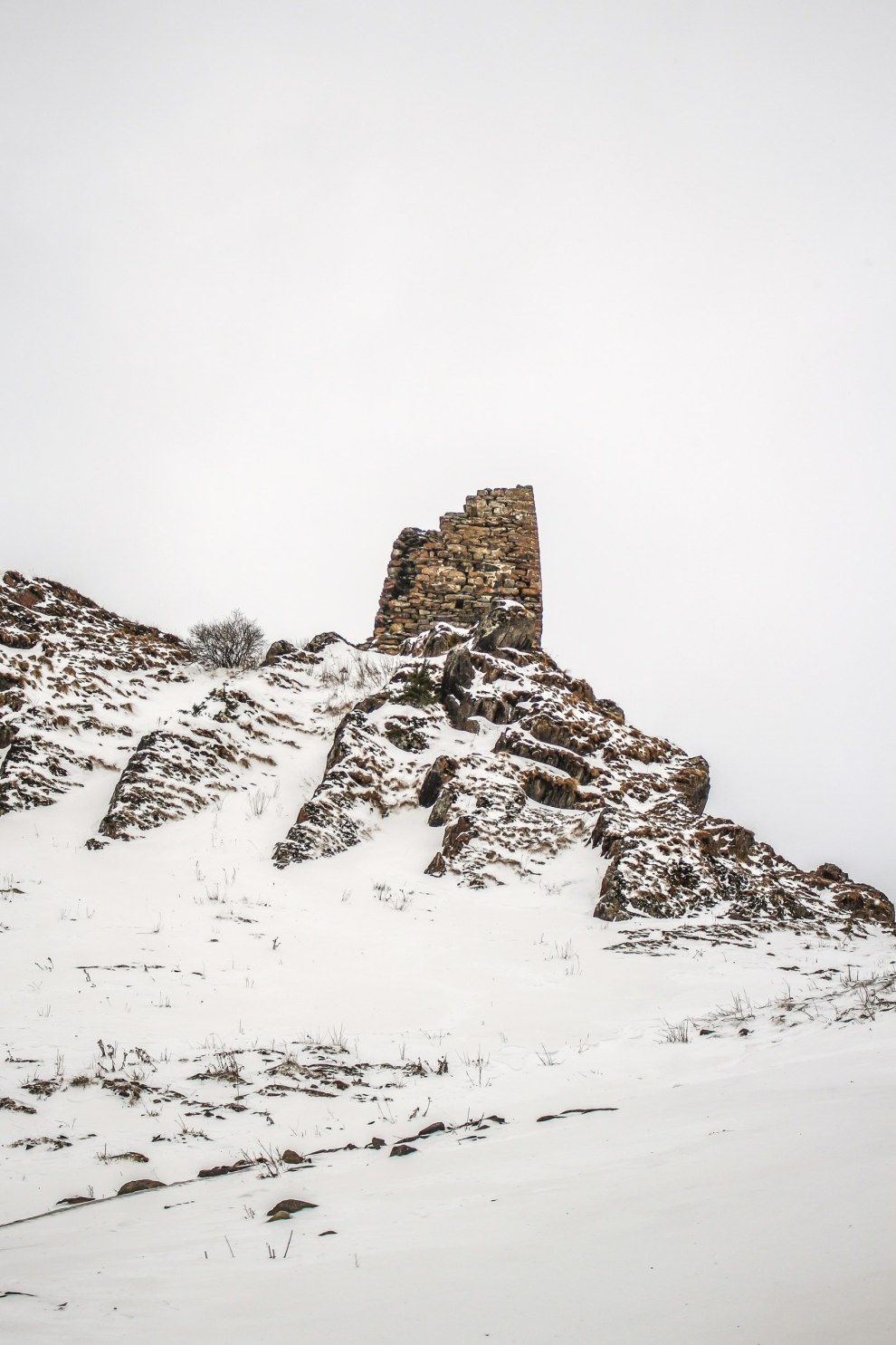 Ruined stone tower on a snowy rocky slope near Kazbegi, Georgia