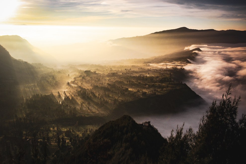 Misty volcanic landscape around Mount Bromo at sunrise, seen from Cemoro Lawang, Java, Indonesia, with clouds drifting through the valleys