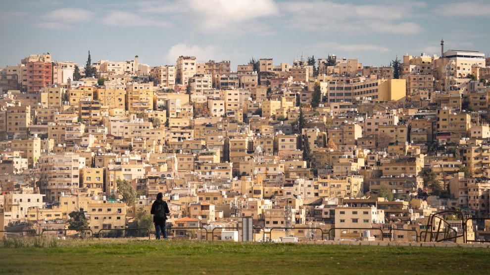 Person standing on a lawn in front of densely built hillside houses, Amman, Jordan