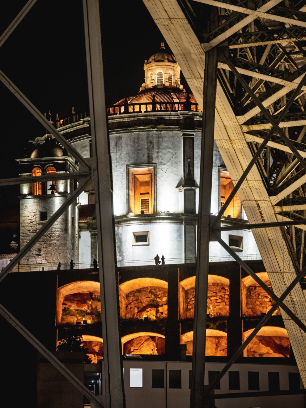 Illuminated historic building at night, framed by dark iron latticework, Lisbon, Portugal