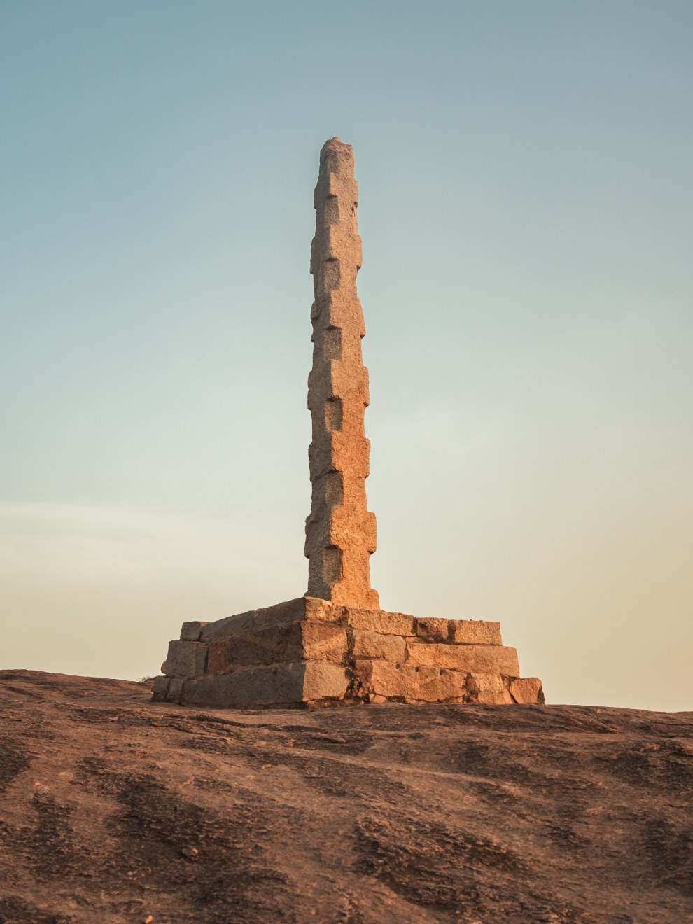 Tall stone pillar on a rocky hilltop in evening light, Hampi, India