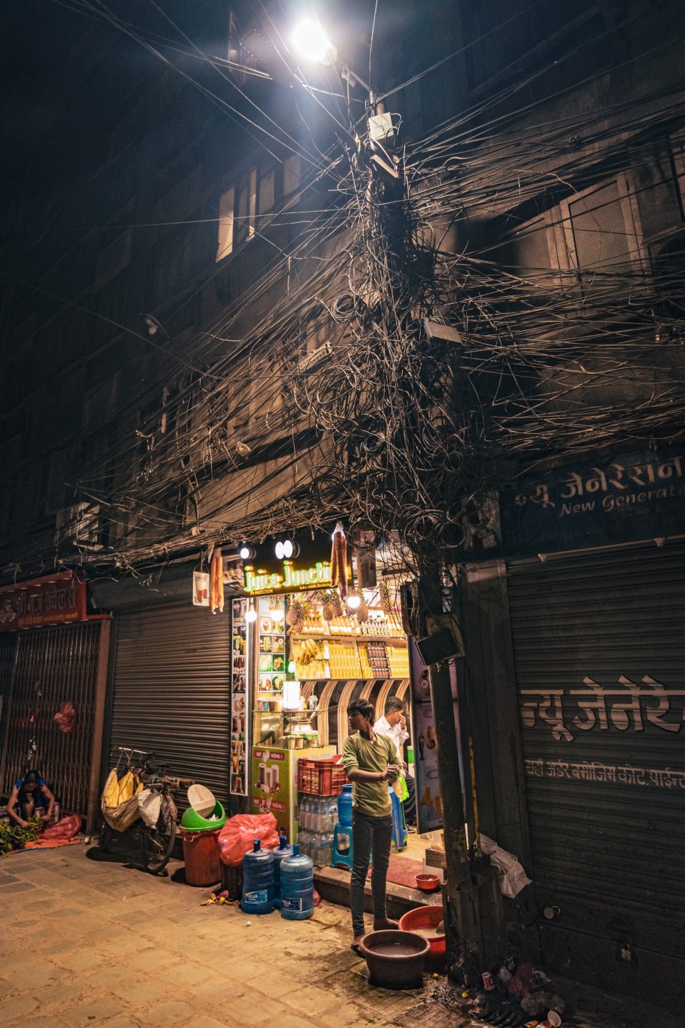 Small shop lit by a street lamp beneath a tangle of electric cables at night, Kathmandu, Nepal