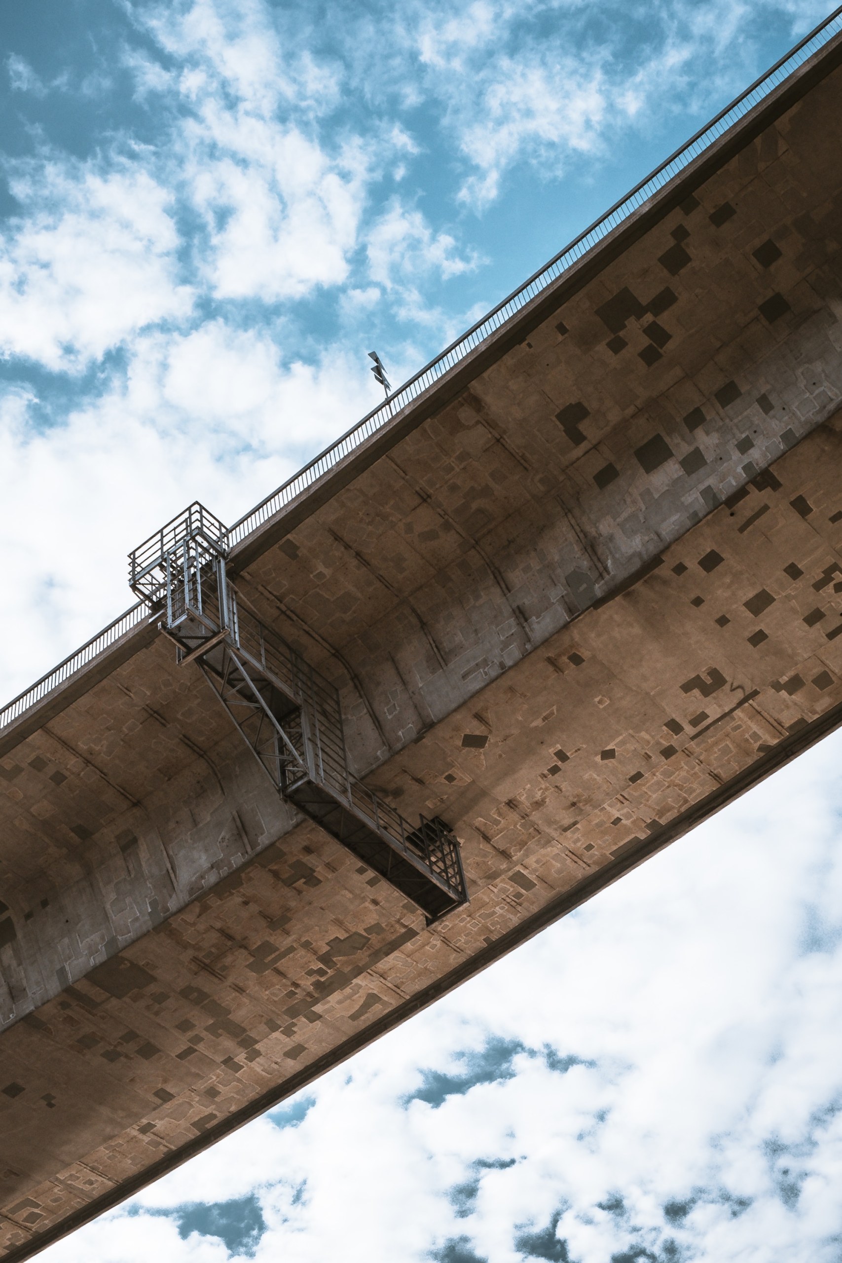 Underside of the Köhlbrand Bridge with a steel maintenance stairway against a cloudy blue sky in Hamburg-Wilhelmsburg