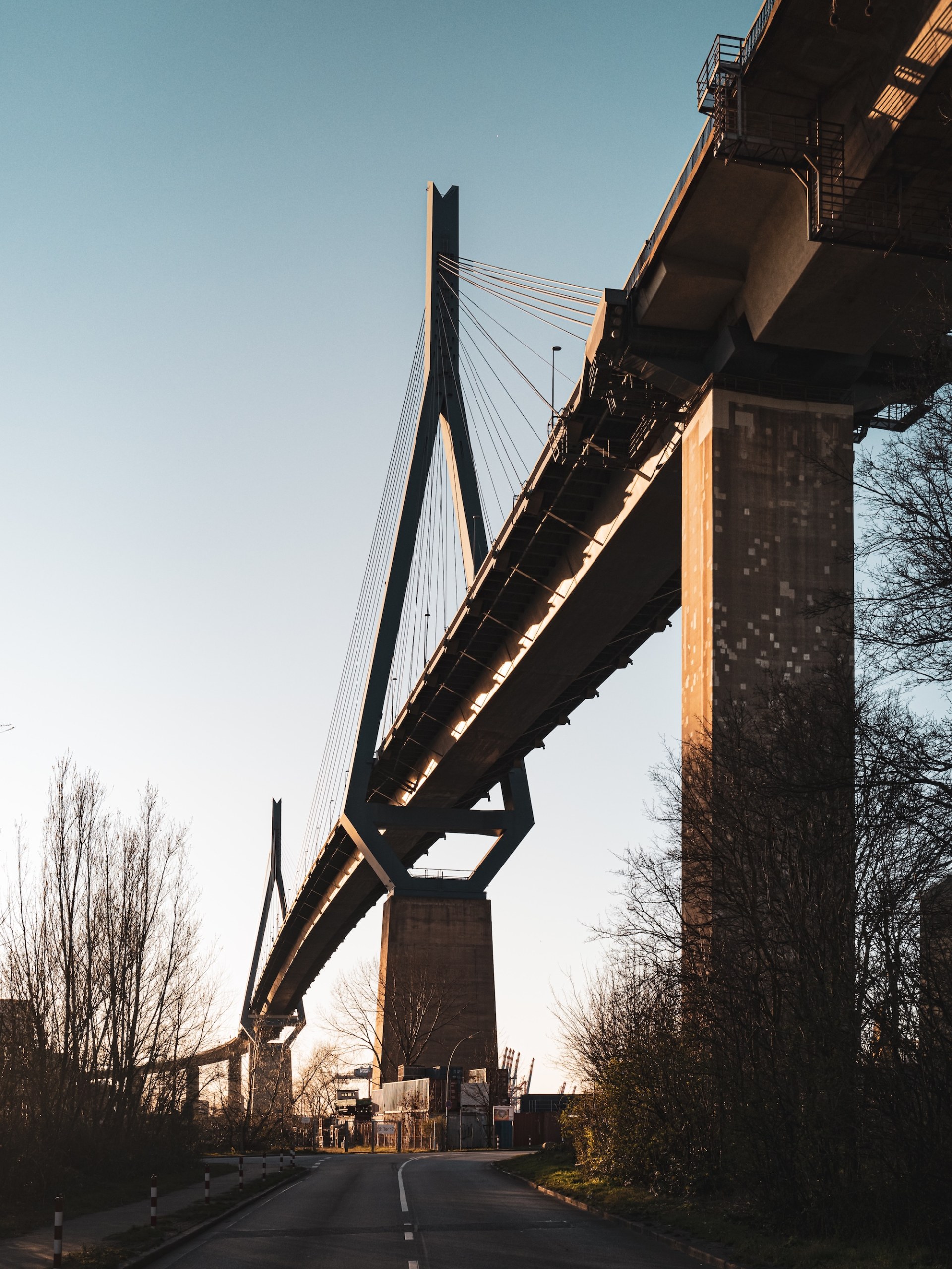 Köhlbrand Bridge in Hamburg-Wilhelmsburg seen from below in evening light, with its pylons and a concrete pier above an empty road