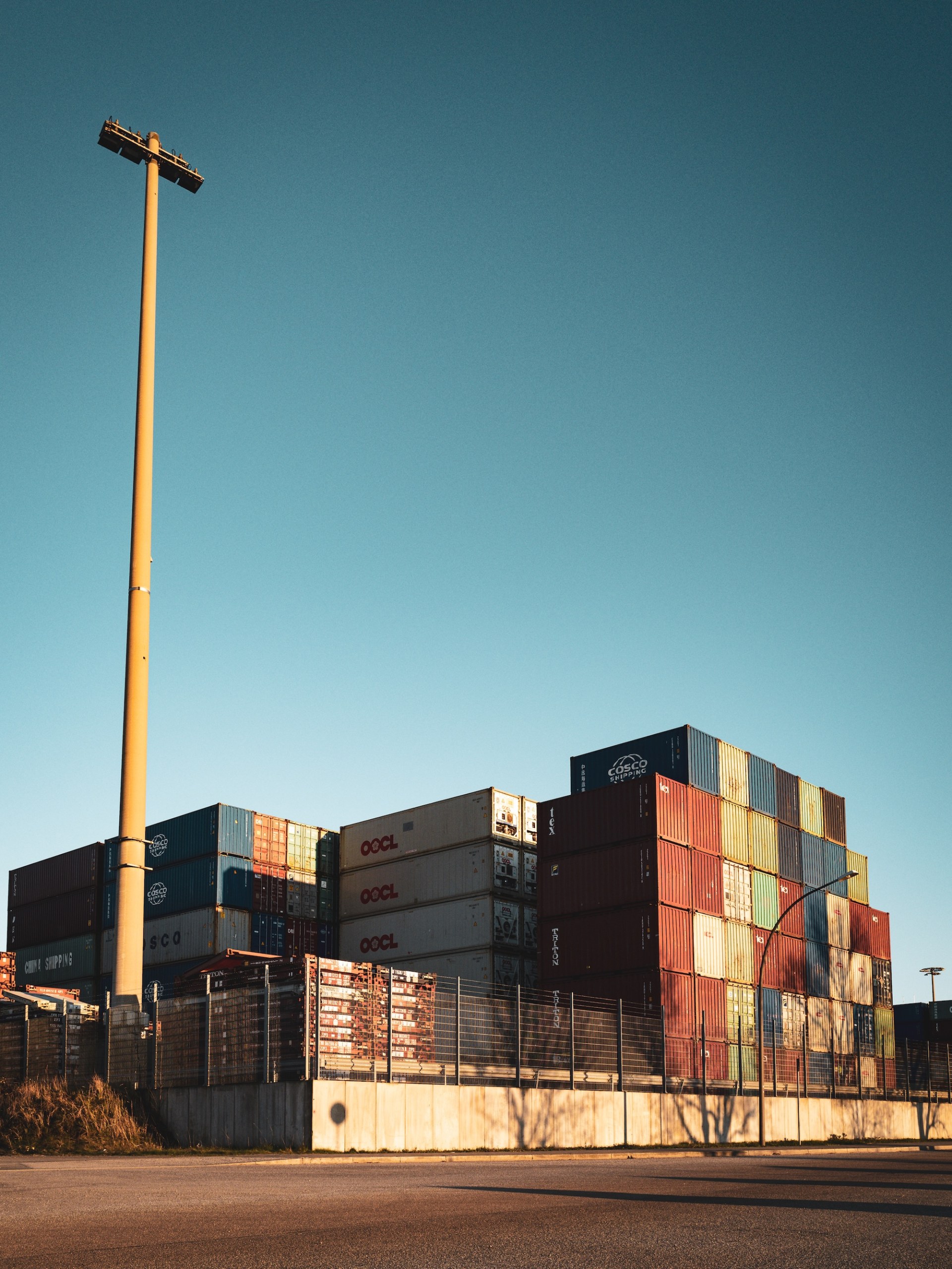 Stacked shipping containers and a tall floodlight mast in evening light in the port of Hamburg-Wilhelmsburg