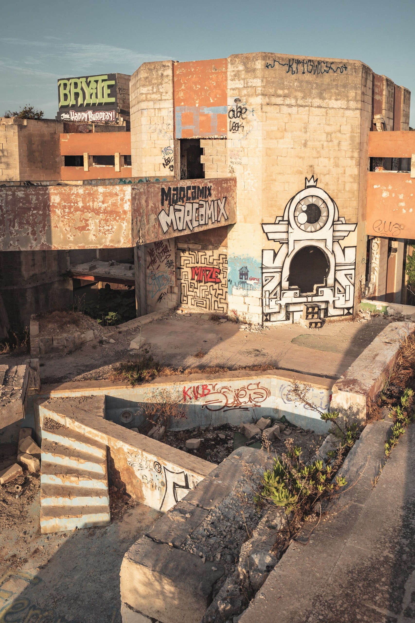 Ruined concrete building covered in graffiti and murals above an empty, derelict basin with steps