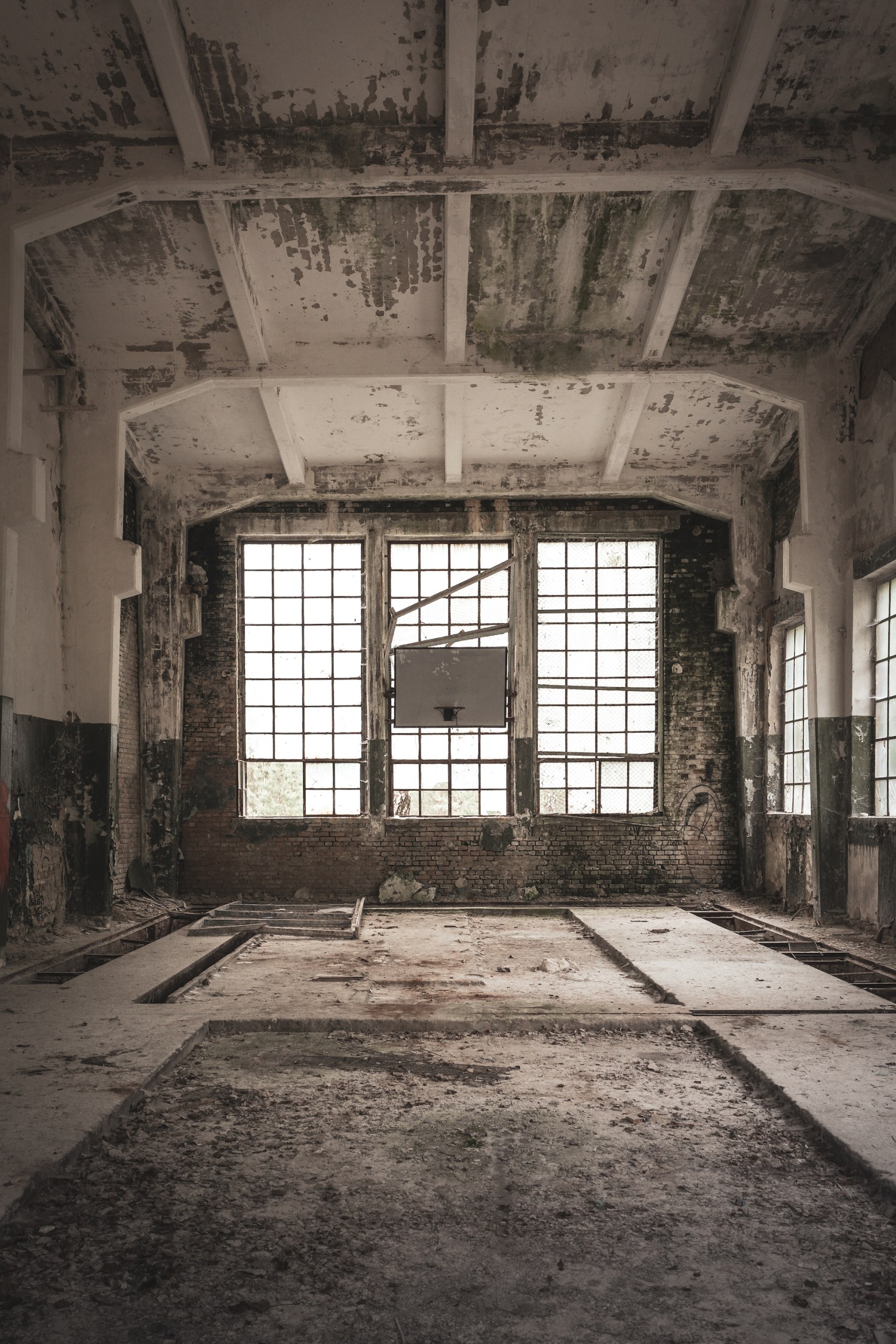 Abandoned gymnasium with a basketball hoop in front of large windows