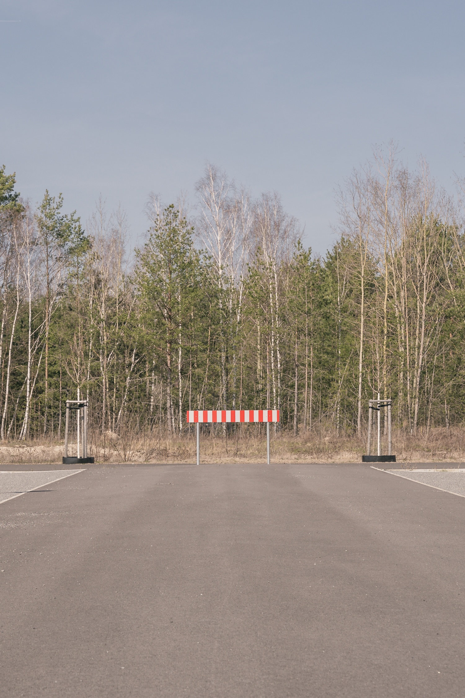 Red-and-white barrier at the end of an empty, newly built road in front of a young forest in Lusatia