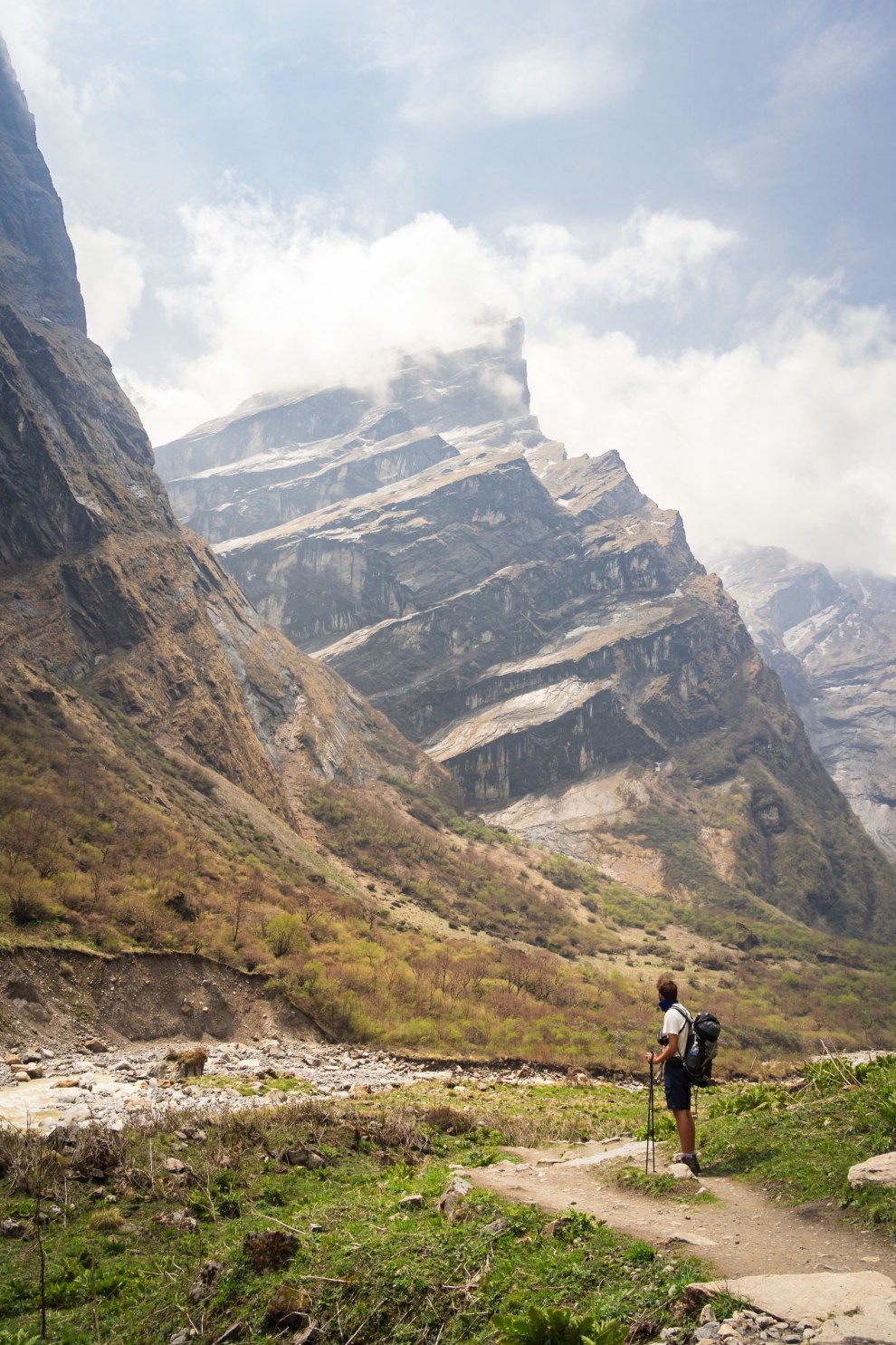 Hiker standing on a trail beneath towering rock walls and cloud-capped peaks in the Annapurna region, Nepal
