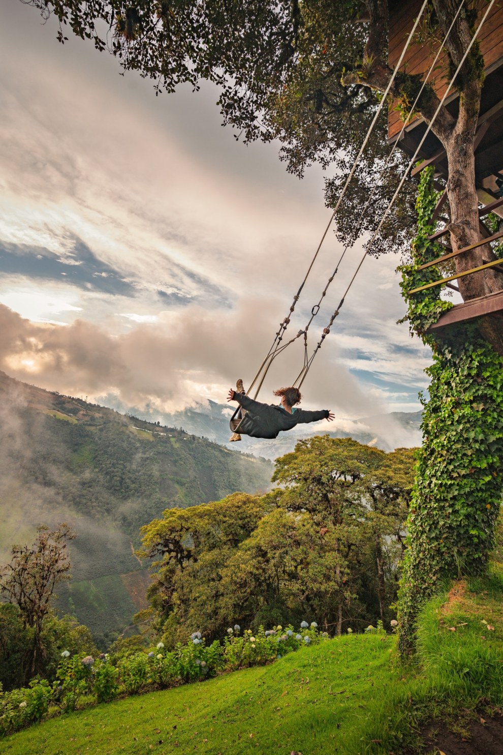 Person on a giant swing soaring over a misty green valley in Baños, Ecuador