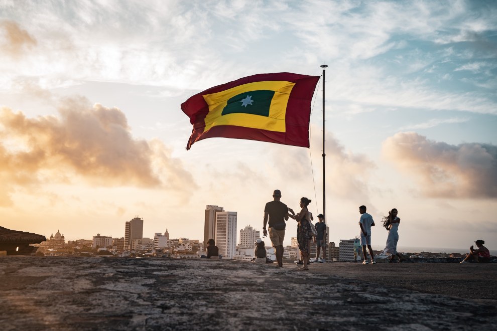 People and a large flag on the city walls at sunset with the skyline behind, Cartagena, Colombia