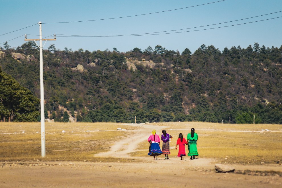 Women in brightly coloured traditional dresses walking along a dirt road in Chihuahua State, Mexico