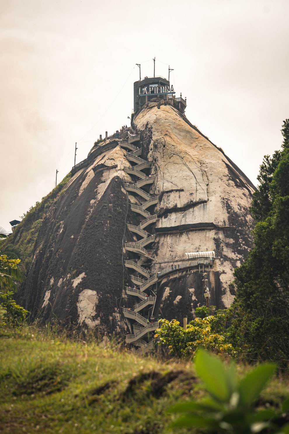 The monolith of El Peñol with its zigzag staircase rising above green vegetation in Guatapé, Colombia