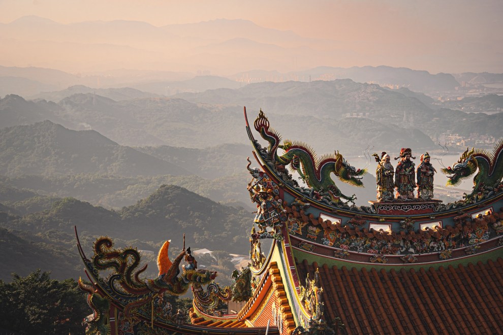 Ornate dragon roof of a temple in front of misty layered hills at dusk, Jiufen, Taiwan