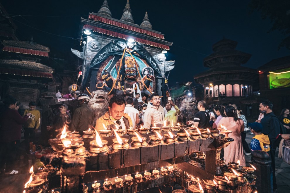 Rows of burning oil lamps in front of an ornate temple at night with worshippers, Kathmandu, Nepal