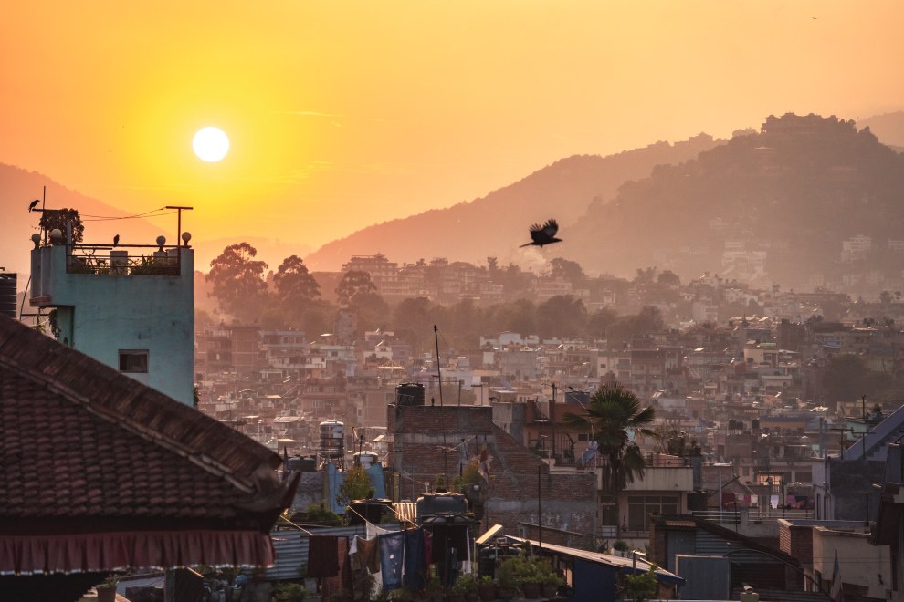 Sun rising over the hazy rooftops and hills of Kathmandu as a crow flies past, Nepal