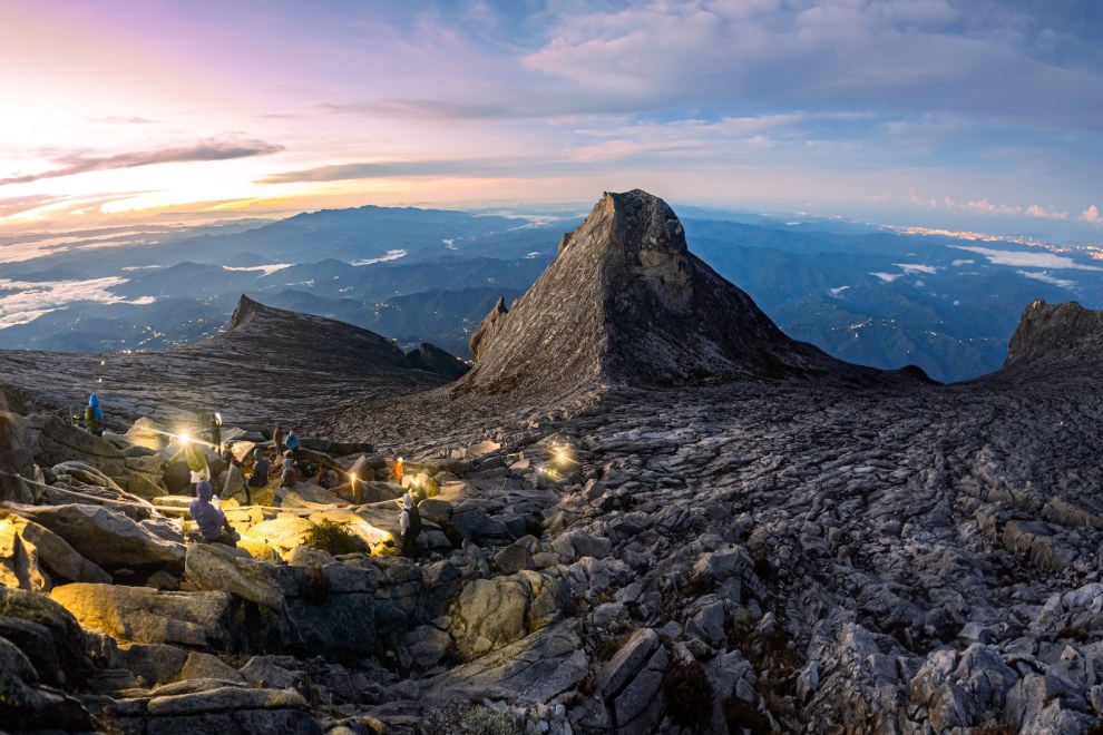 Headlamps of climbers on the granite summit plateau of Mount Kinabalu at dawn above a sea of clouds, Malaysia