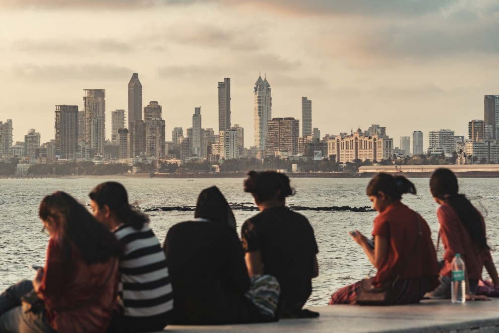 Group of women sitting on a sea wall looking towards the hazy Mumbai skyline, India