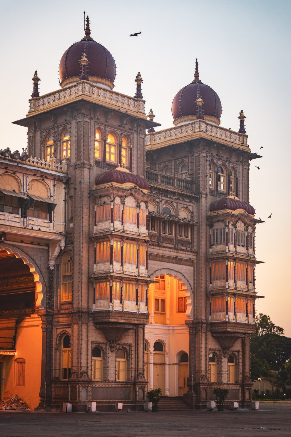 Twin domed towers of Mysore Palace glowing in the evening light as birds fly overhead, India