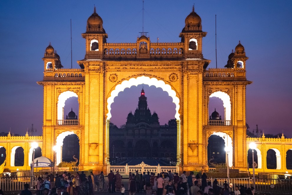 Illuminated golden gate of Mysore Palace at dusk with the palace visible through the arch, India