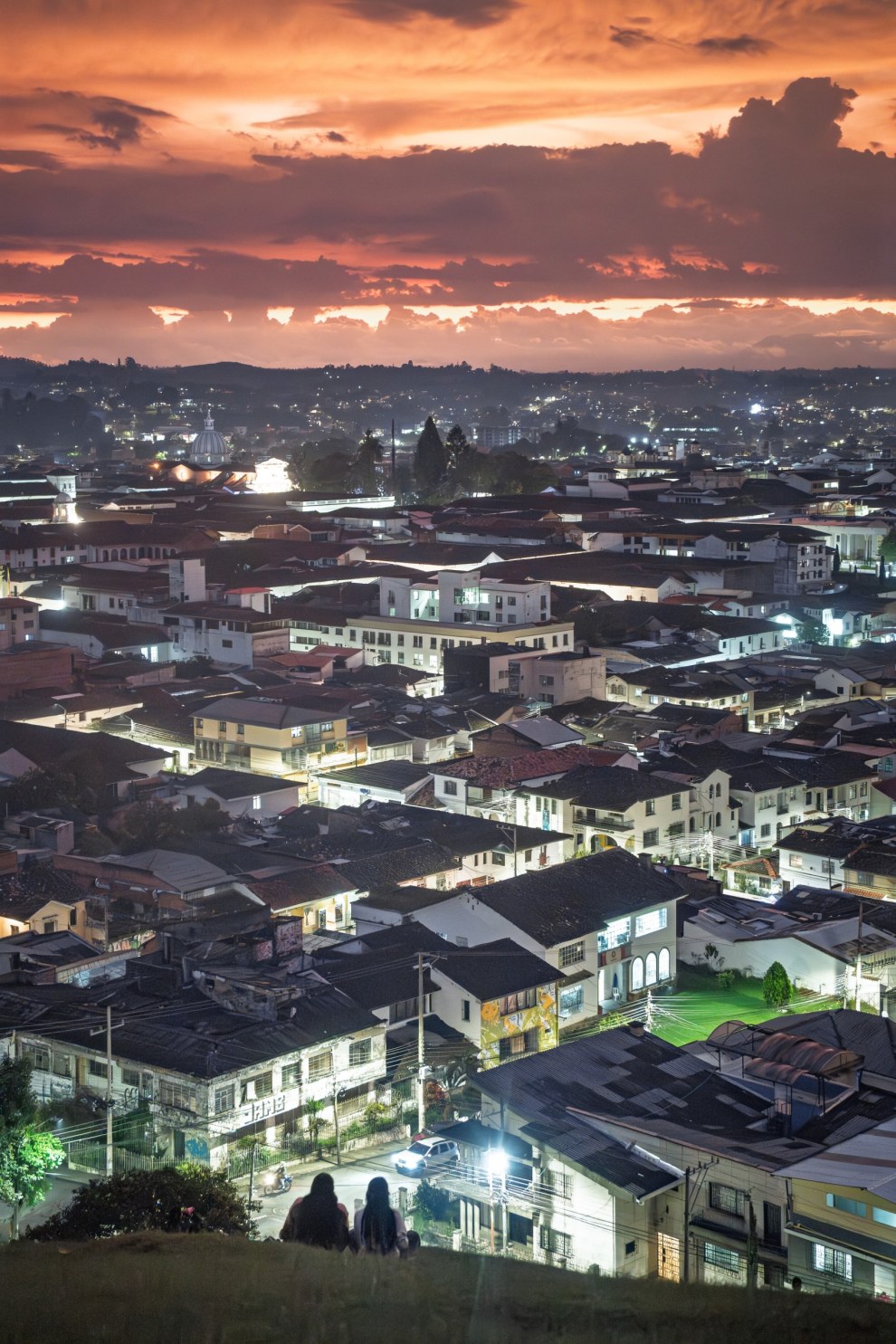 Two people looking out over the lights of Popayán beneath a glowing sunset sky, Colombia