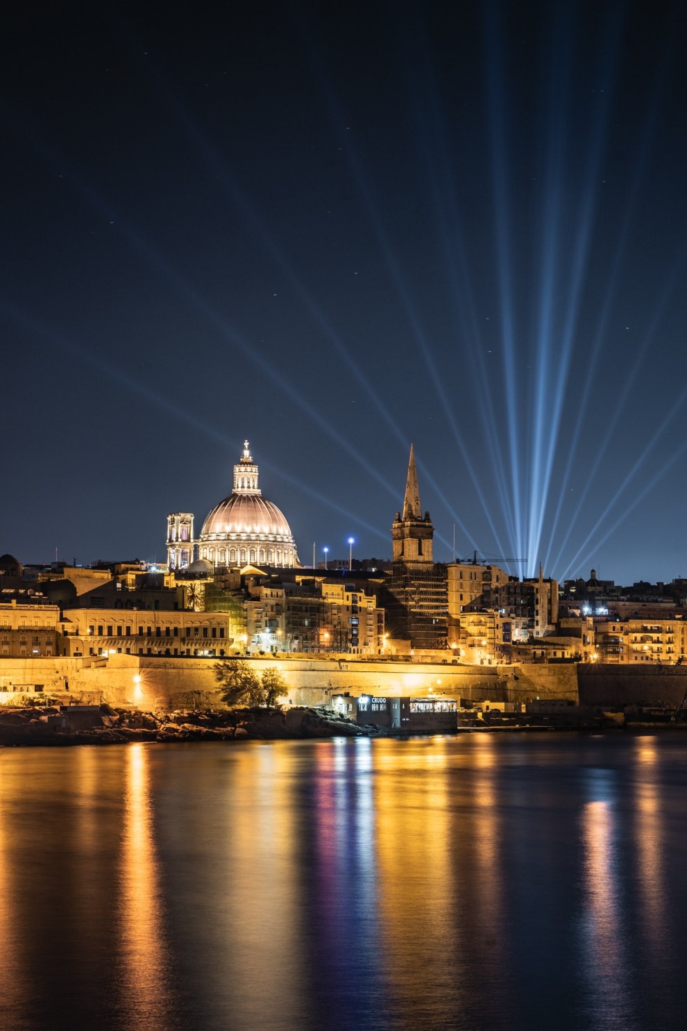 Valletta skyline with a church dome and searchlights reflected in the harbour at night, Malta