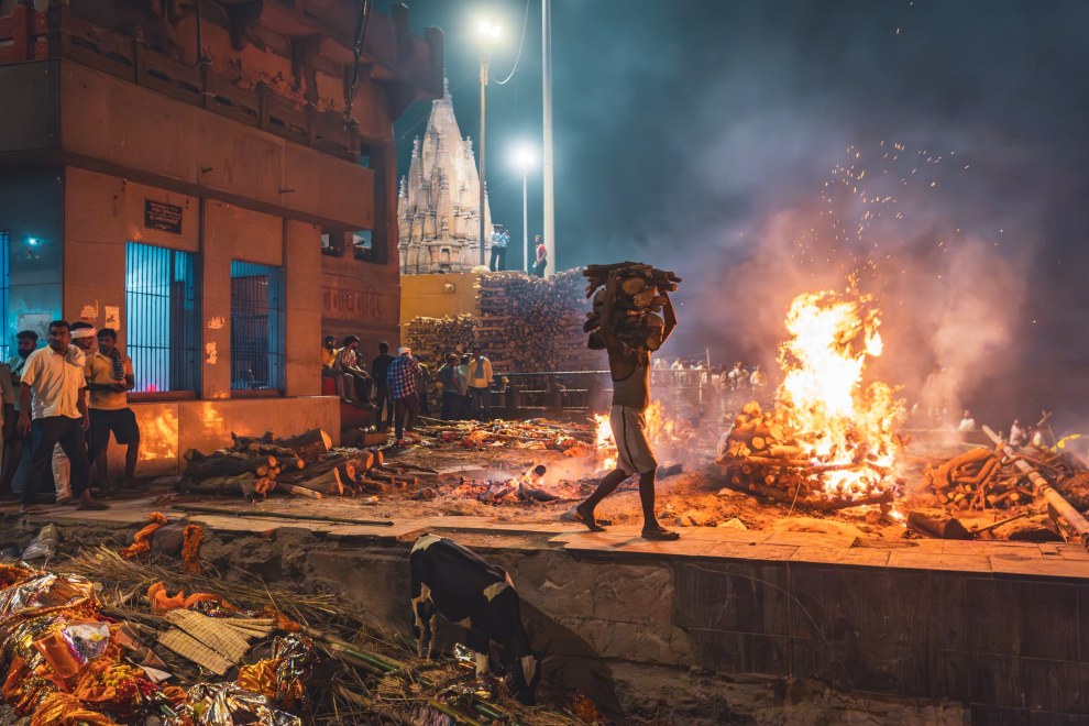 Man carrying wood past a burning cremation pyre at night on the Manikarnika Ghat in Varanasi, India