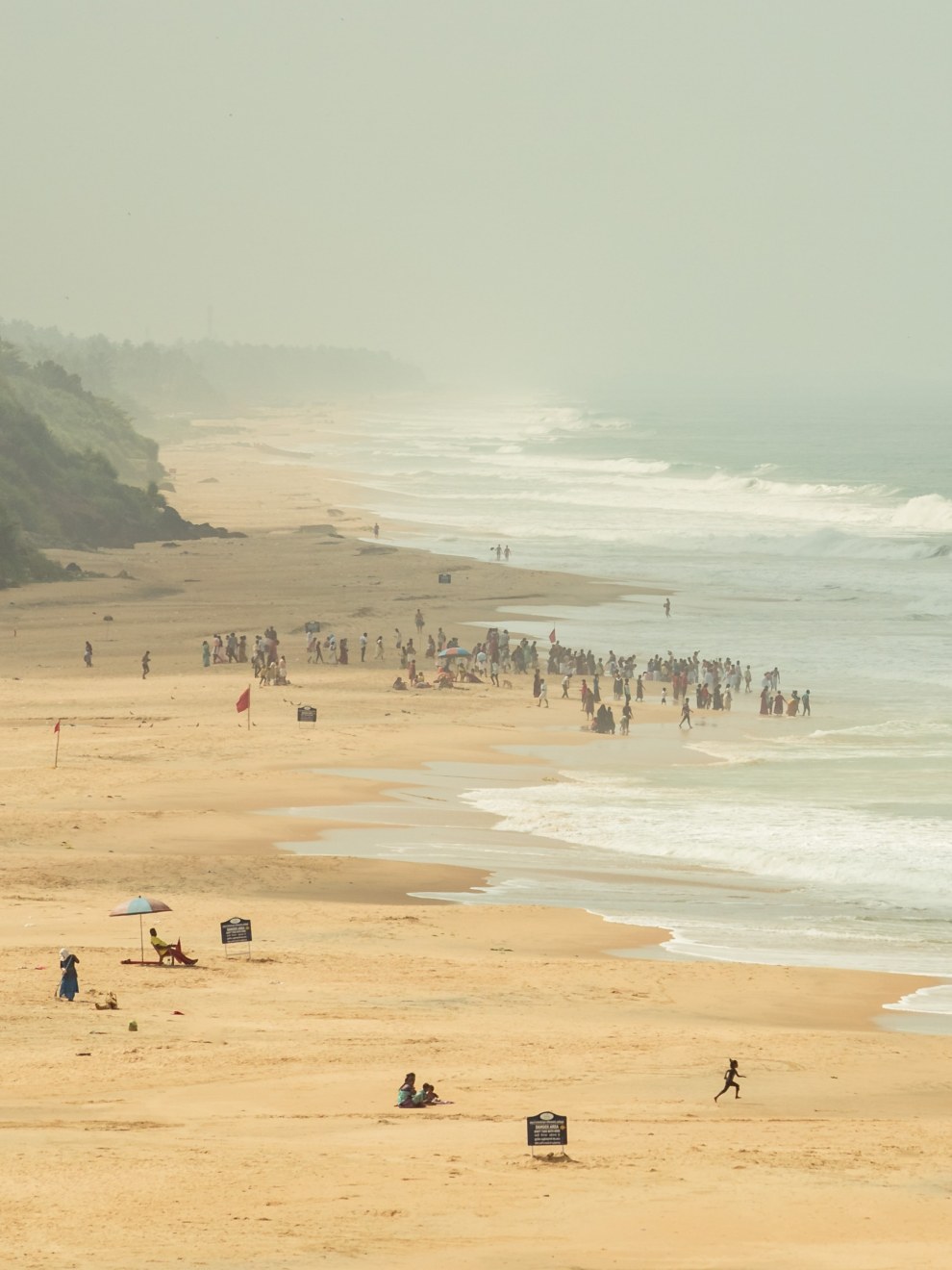 Long hazy beach with groups of people at the water's edge in Varkala, India