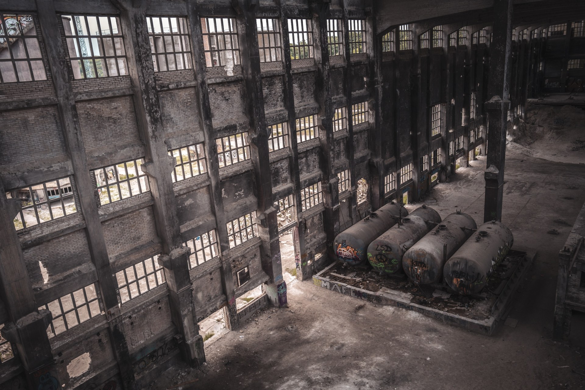 Huge empty factory hall with tall window walls and four abandoned tanks, Rüdersdorf, Germany