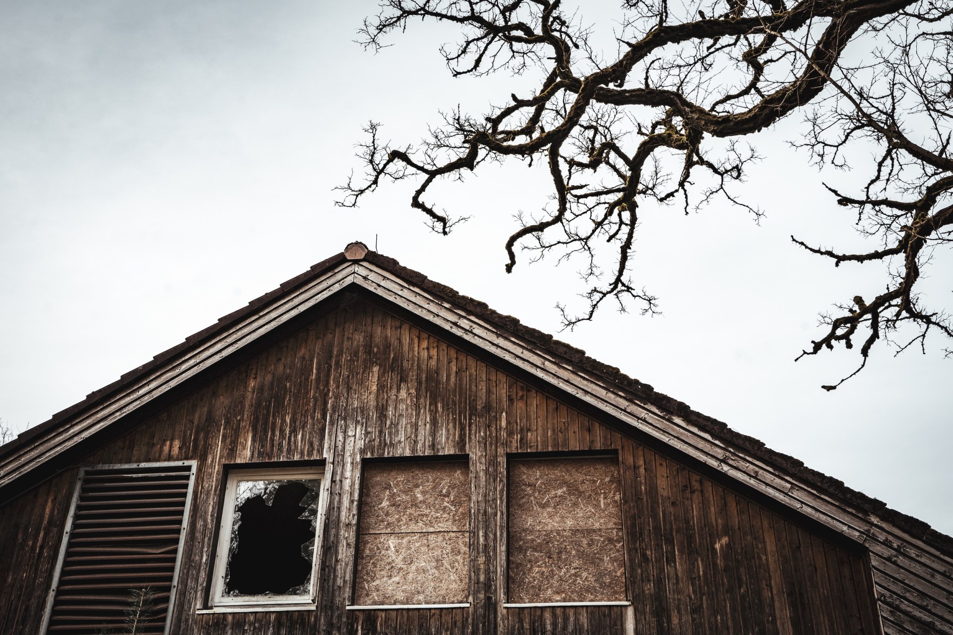Weathered wooden gable with a broken window beneath bare branches, near Hamburg, Germany