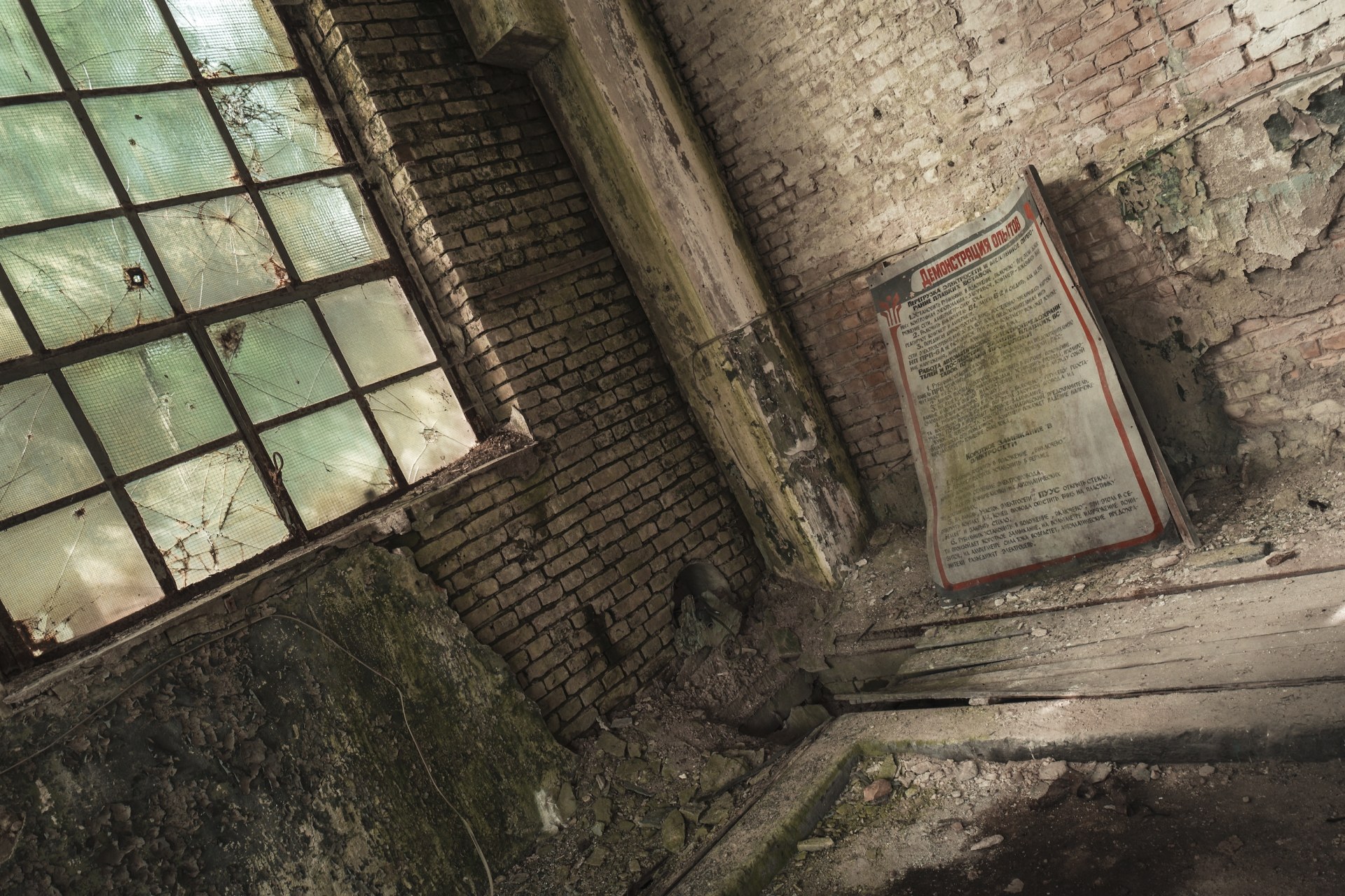 Old Russian-language poster leaning against a brick wall beside a broken window, Kummersdorf, Germany