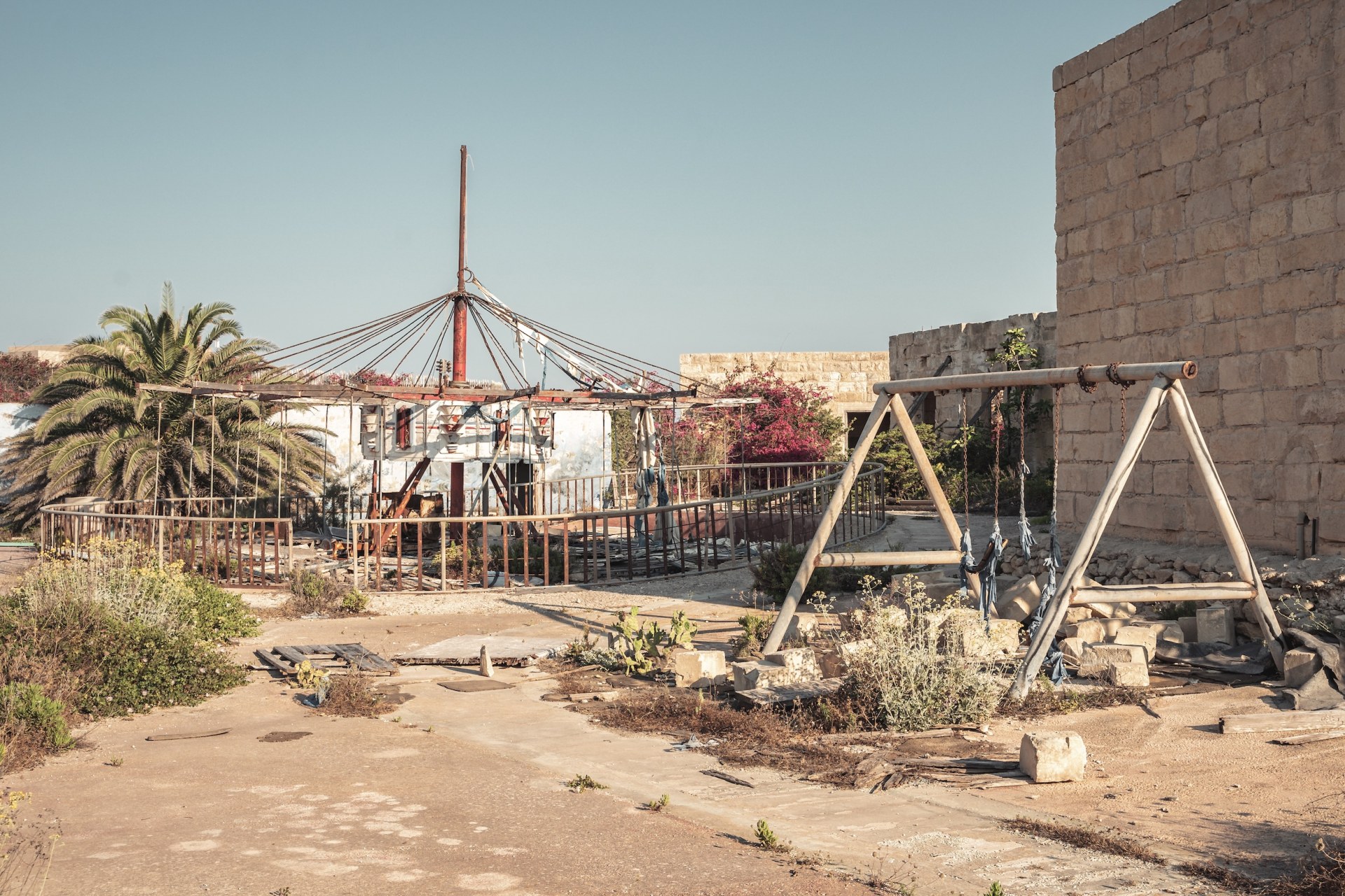 Derelict carousel and swing frame on a sandy lot, Rinella Movie Park, Malta