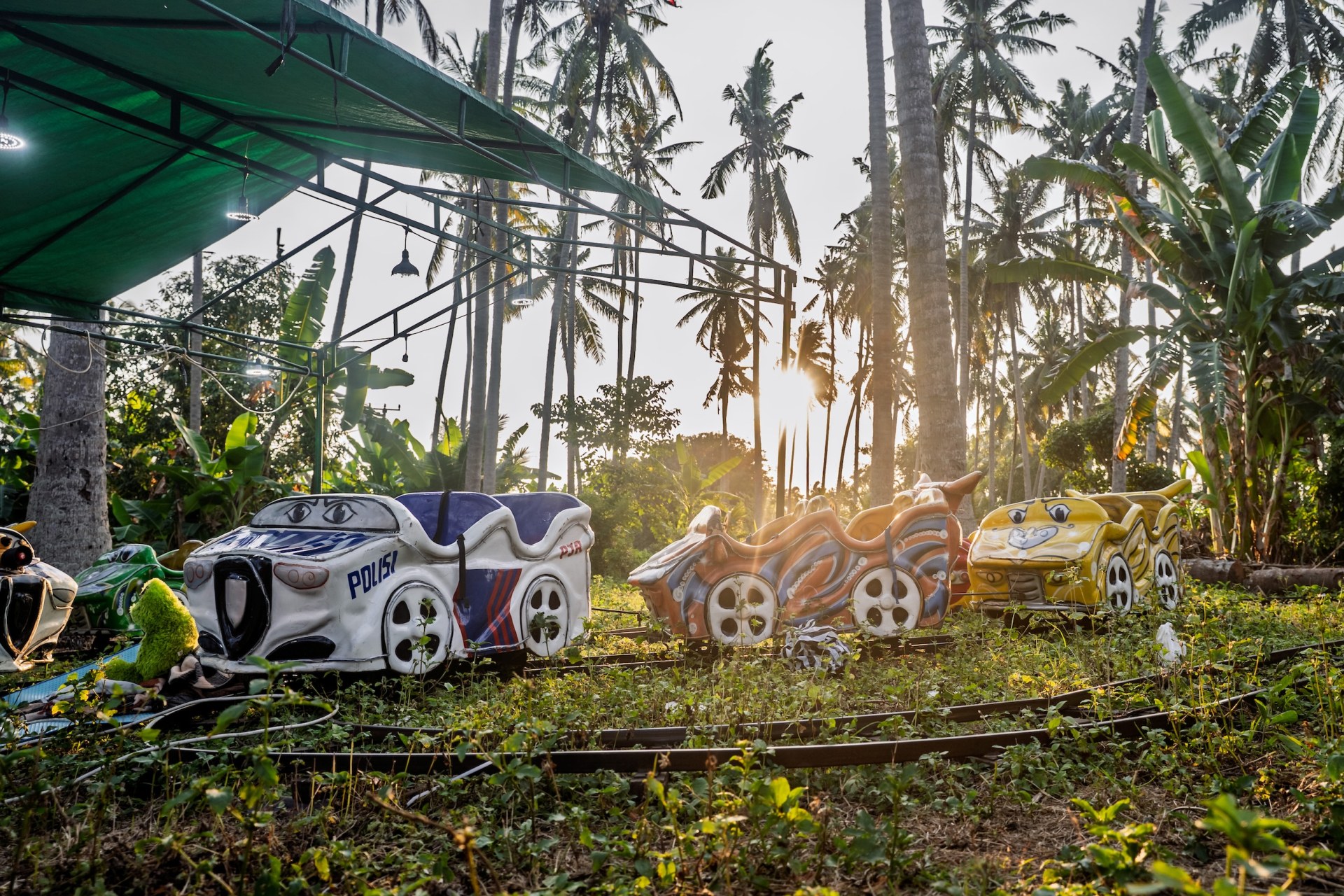 Children's ride cars on overgrown tracks under palm trees in backlight, Nusa Penida, Indonesia