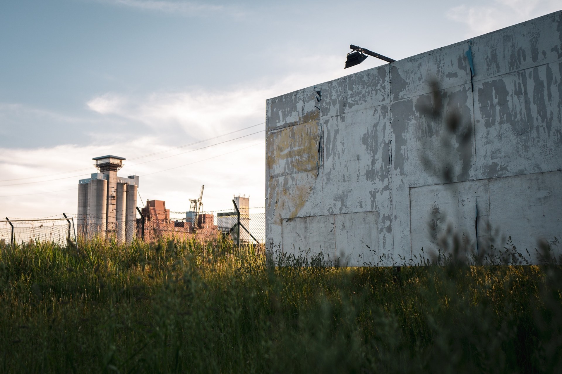 Weathered wall with a floodlight in tall grass, the Rethespeicher silo in the background, at the deserted MS Dockville festival site, Hamburg-Wilhelmsburg, Germany, summer 2020