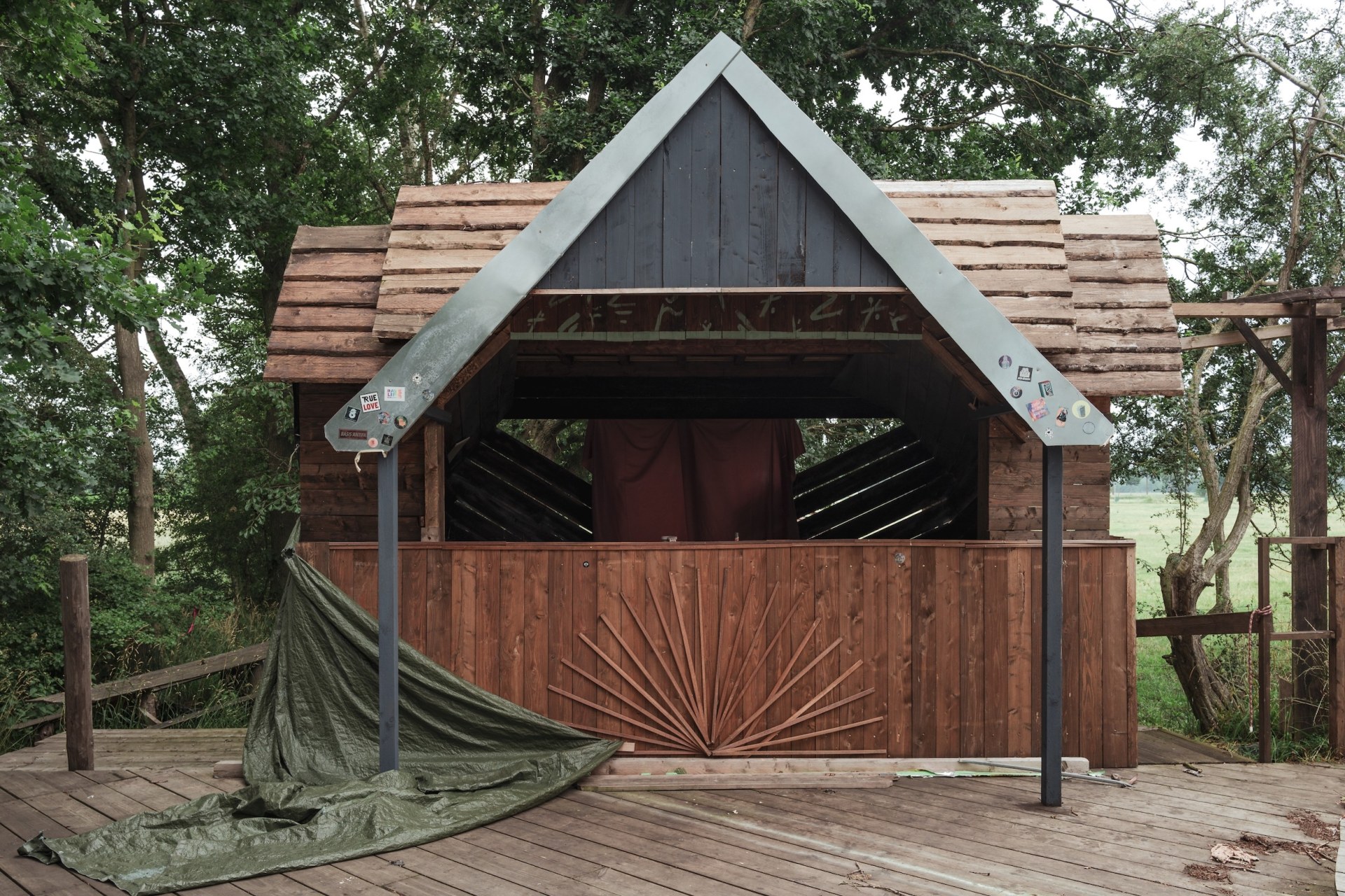 Empty wooden pavilion with a gabled roof and a fallen tarpaulin at the deserted MOYN festival site, near Oyten, Germany, summer 2020