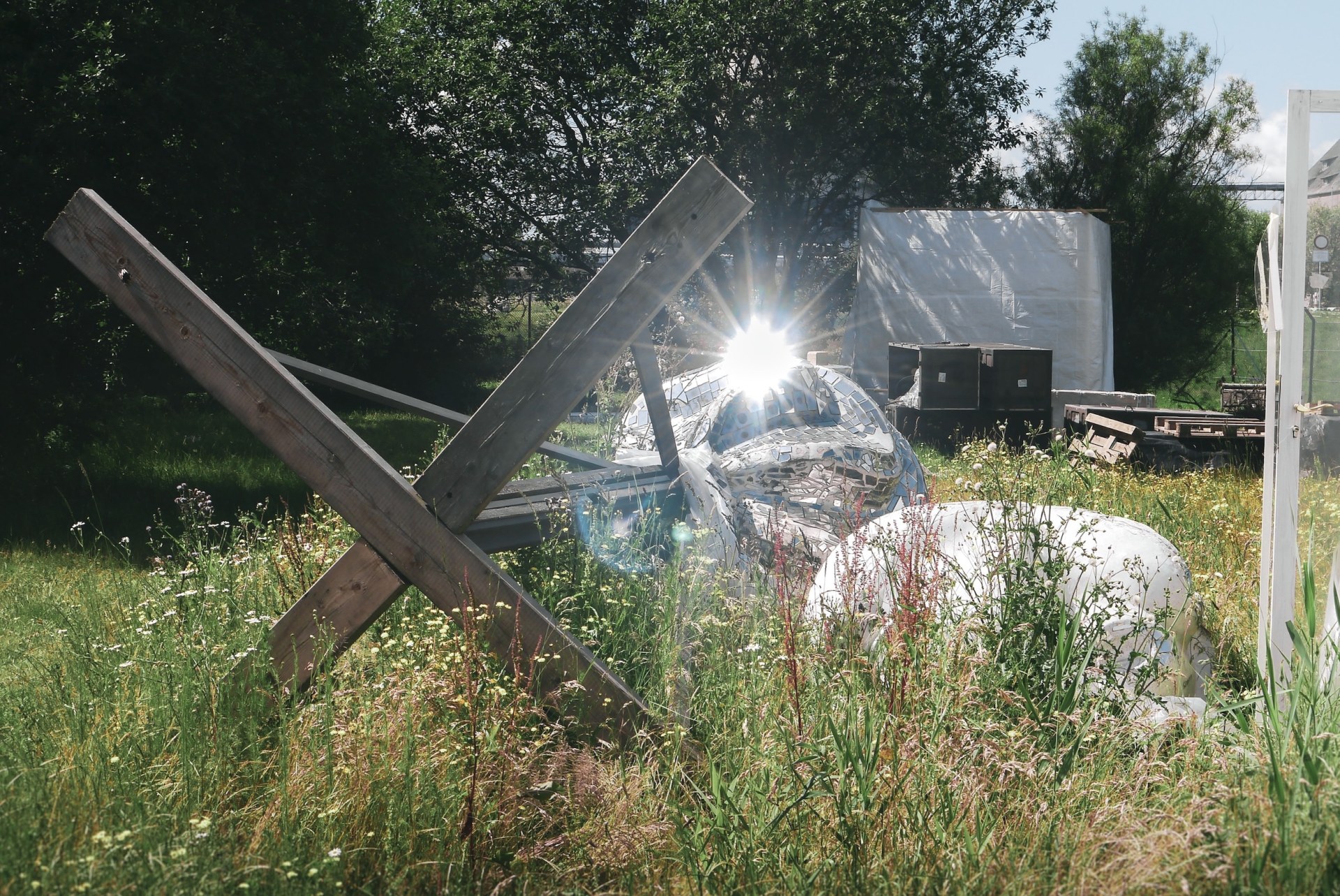 Crossed wooden beams and a disco ball sculpture glinting in the sun in tall grass at the deserted MS Dockville festival site, Hamburg-Wilhelmsburg, Germany, summer 2020