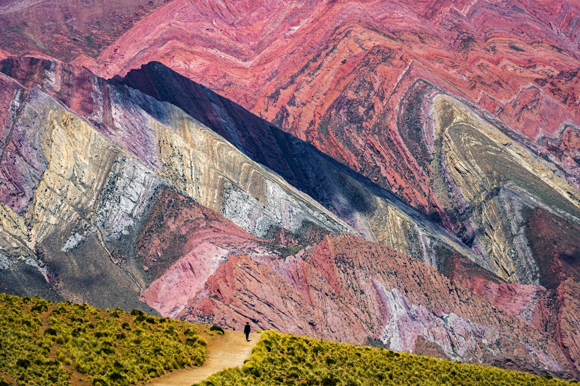 Lone hiker on a path beneath the striped, multicoloured mountain slopes of the Serranía de Hornocal, Argentina