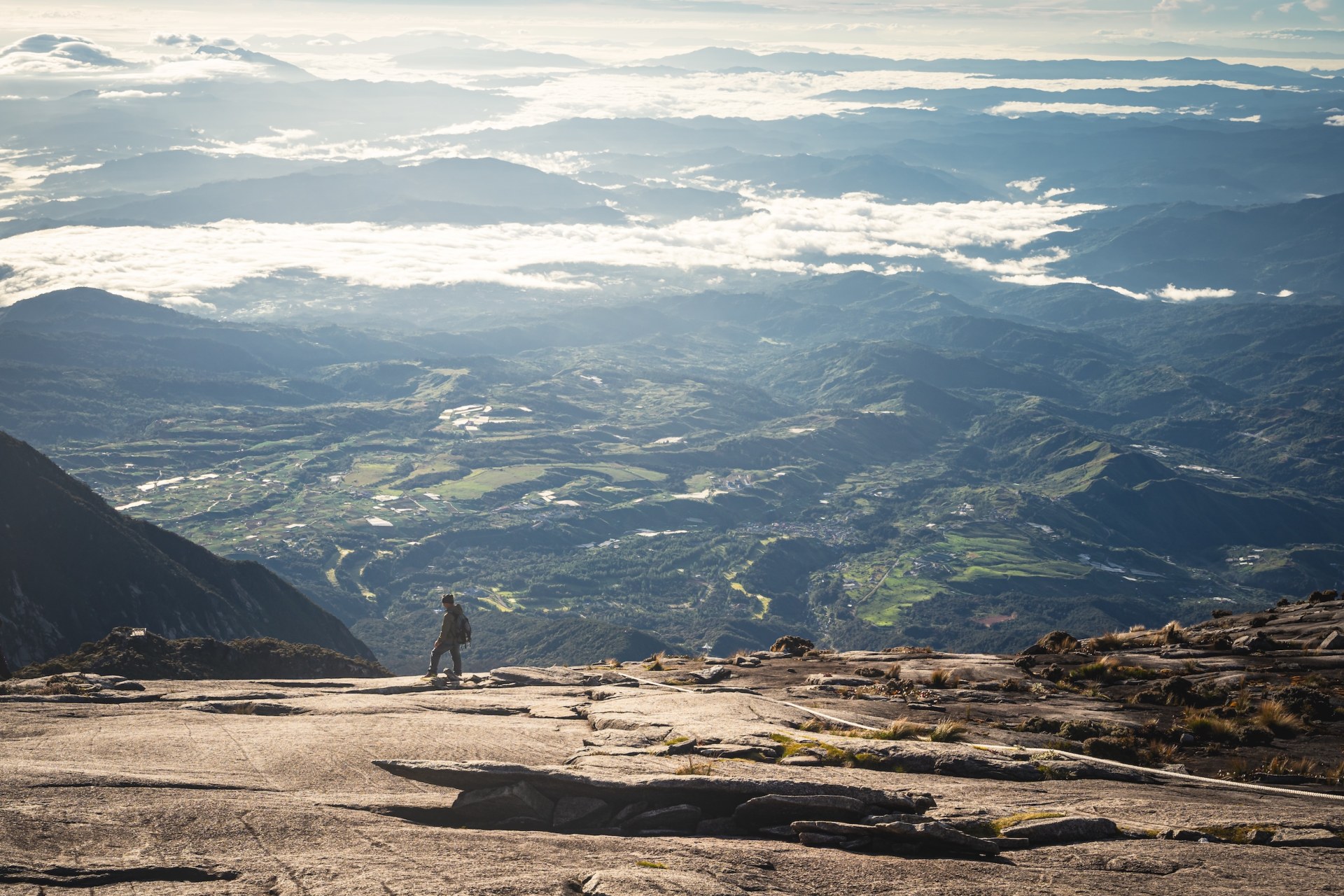 Hiker on the bare granite slopes of Mount Kinabalu above a vast landscape of valleys and clouds, Malaysia