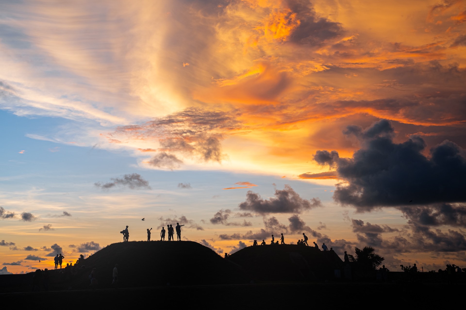 Silhouettes of people on grassy hills against a fiery sunset sky, Galle, Sri Lanka