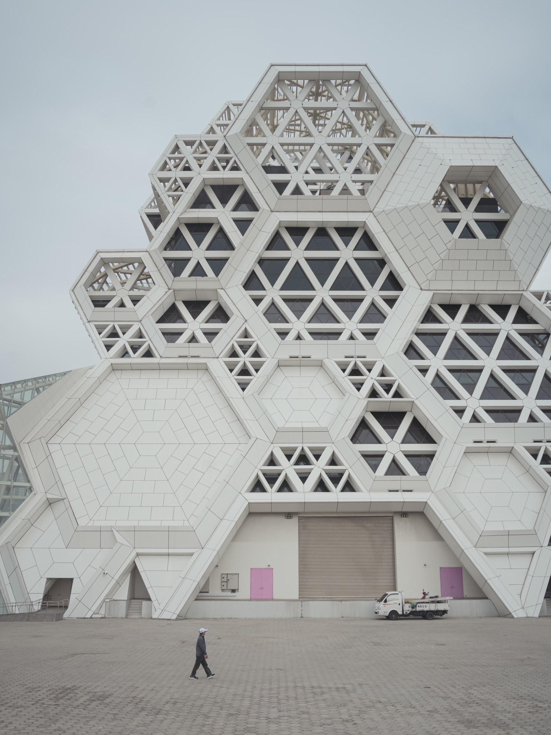 Lone man walking across an empty plaza in front of the white hexagonal facade of the Kaohsiung Music Center, Taiwan