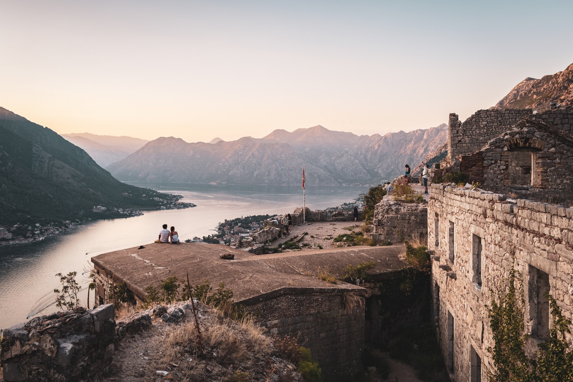 Couple sitting on the walls of an old fortress above the Bay of Kotor at sunset, Montenegro