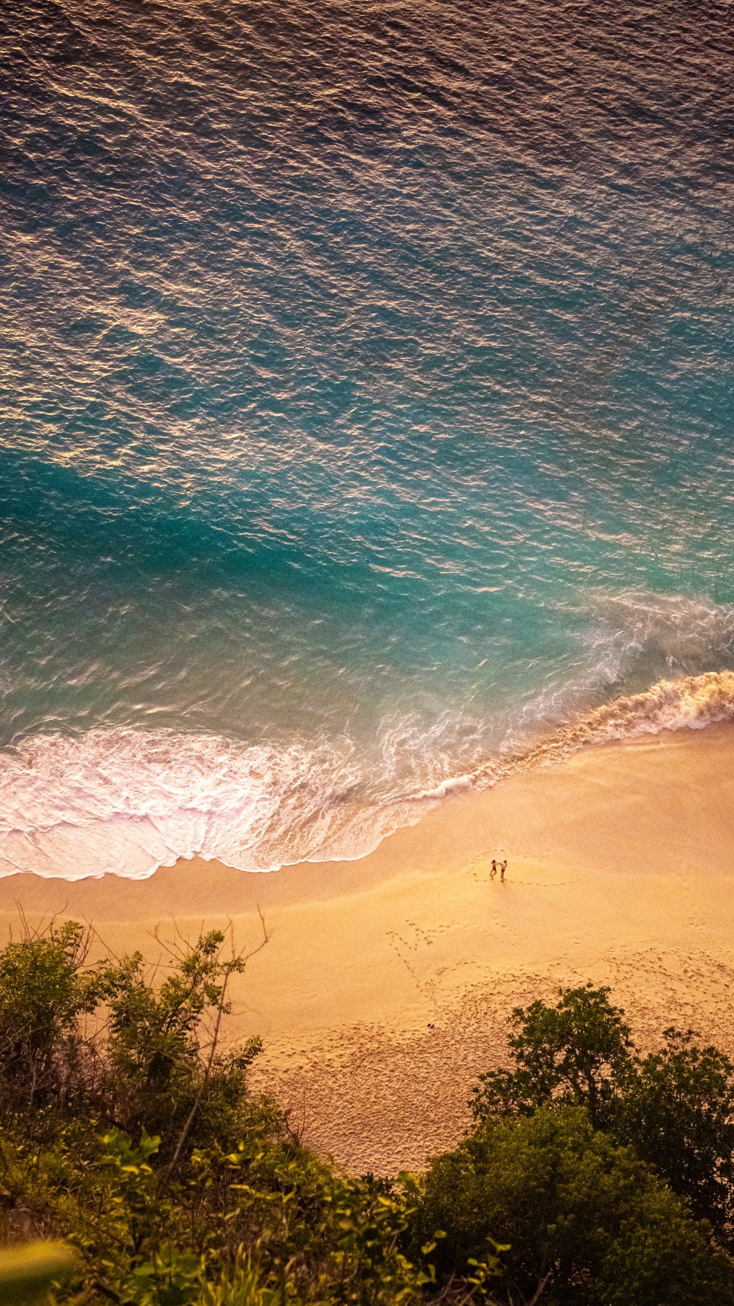 Two people on the beach seen from high above, waves rolling onto golden sand, Kelingking Beach, Nusa Penida, Indonesia